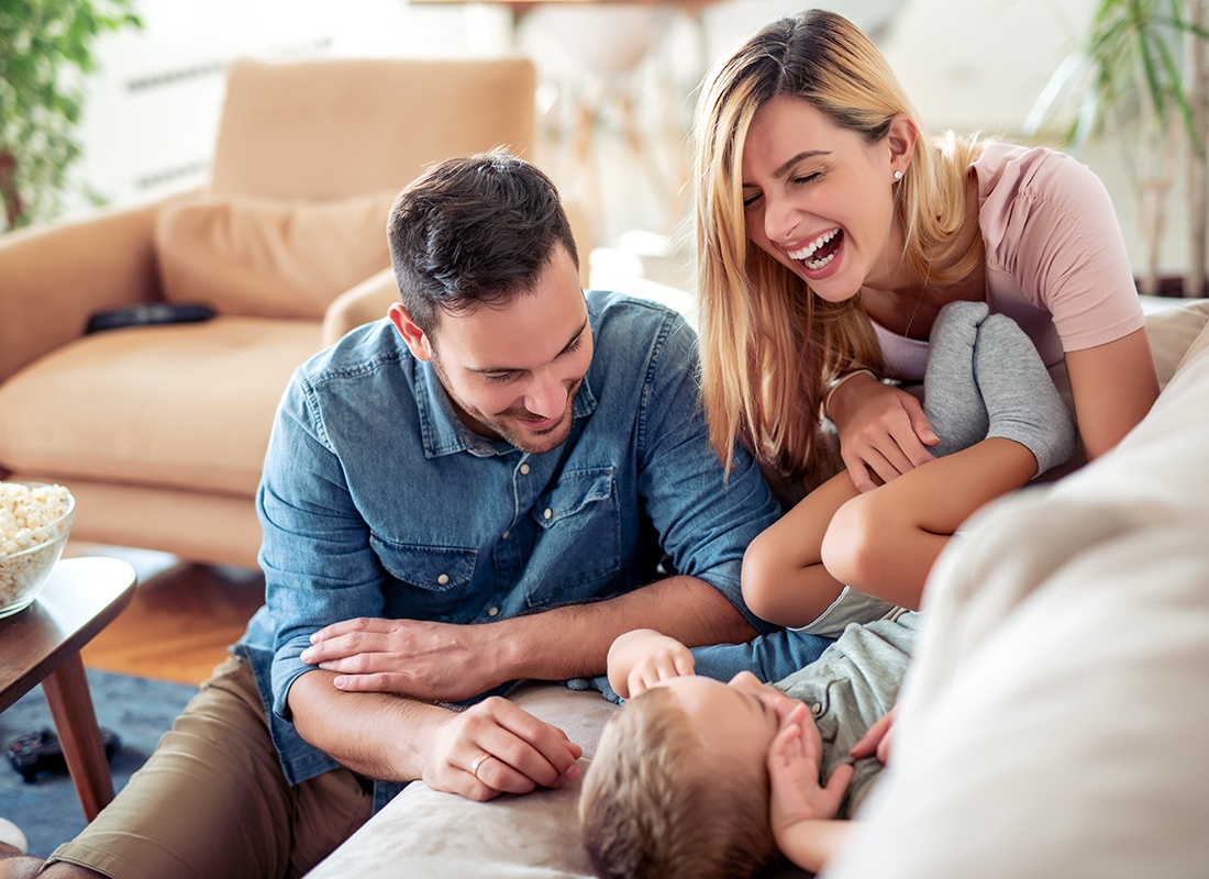 Personal Insurance - Happy Father and Mother Playing With Their Small Child on the Sofa at Home